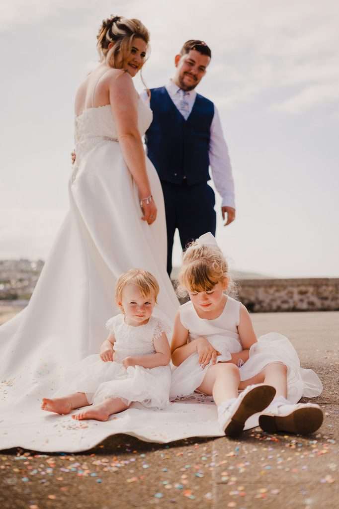 Wedding couple enjoys a moment as their children sit on the wedding dress