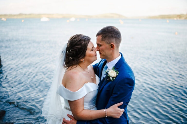 Happy newlyweds lean in for a kiss against the beautiful Cornish sea front - How To Look Your Best In Your Wedding Photos