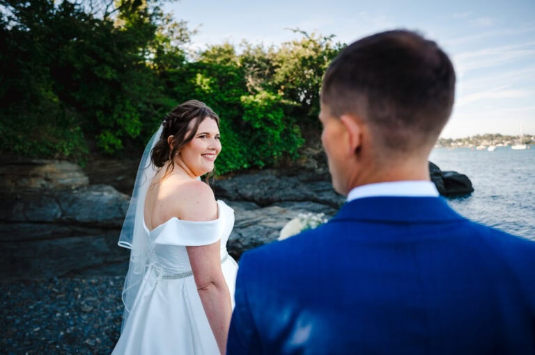 Bride walks along the coast hand in hand as she looks back at her groom - How To Look Your Best In Wedding Photos