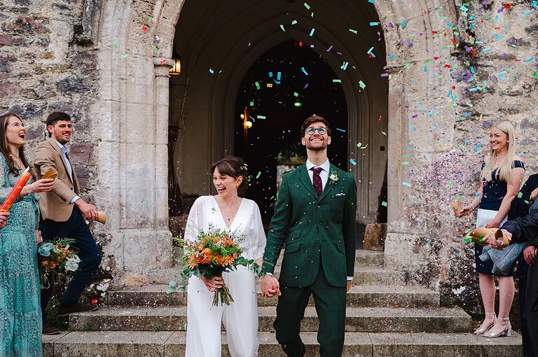 The happy couple walk down the confetti aisle at Dartington hall - Ultimate Wedding Photography Top Tips