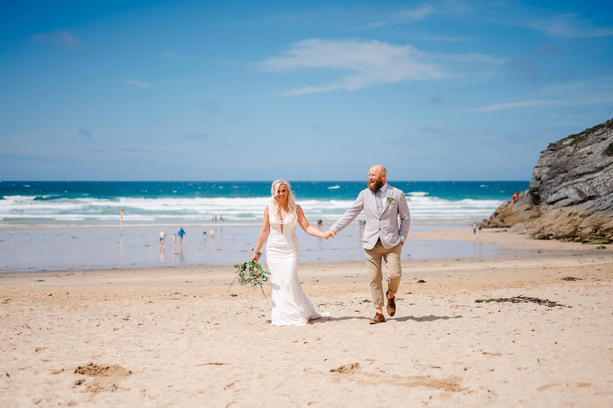 Wedding couple walking along beach happily at Lusty Glaze - Summer Wedding