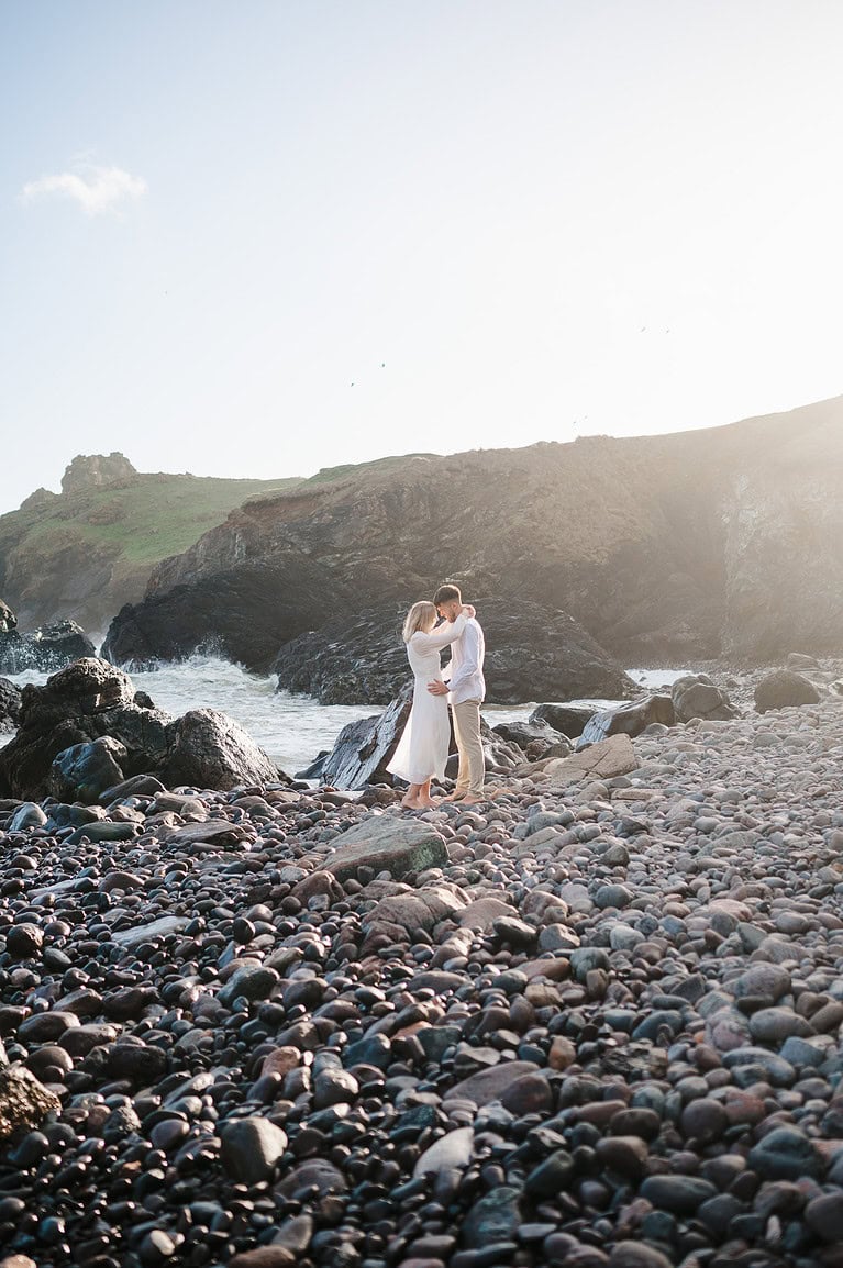 Engagement photo taken at the beautiful Kyncance Cove, Cornwall. The Happy Couple stand on the rocky section of the beach as the suns sets