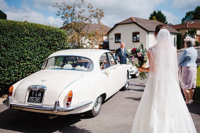 Bride walking up to her classic wedding car, ready to make her wedding entrance in style