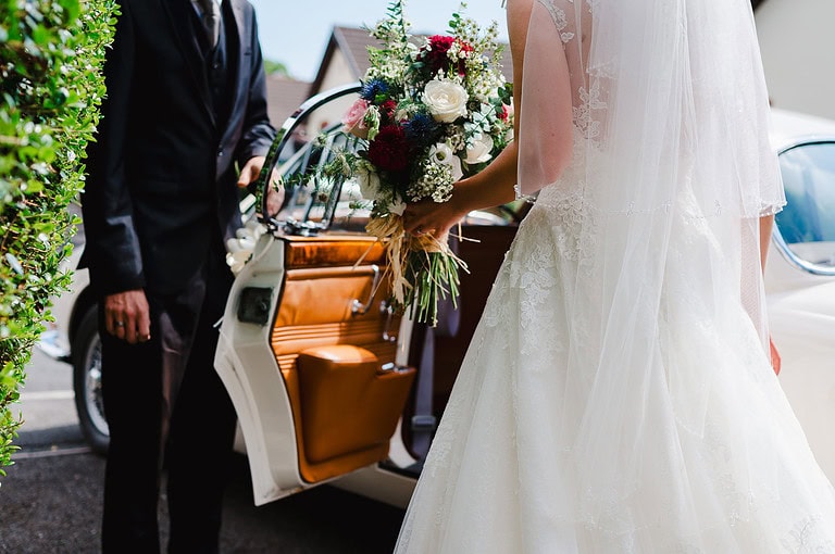 Bride about to get into the wedding car as her driver opens up the car door