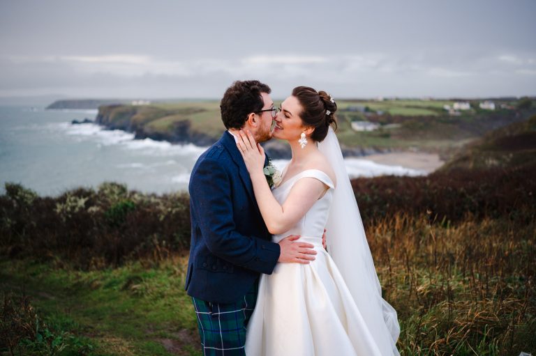 Wedding couple kiss outside their stunning wedding venue by the cliffs in Cornwall - How To Choose The Right Wedding Photographer For You
