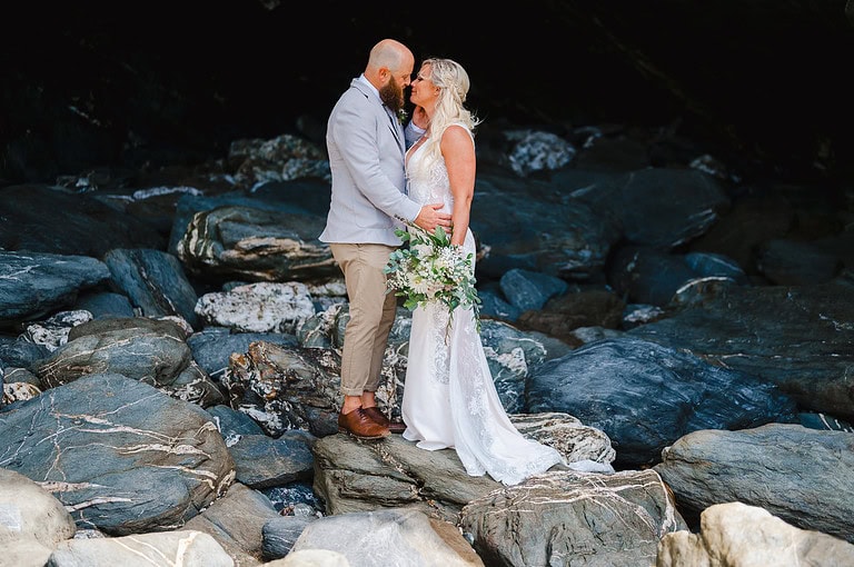 Couple stand on rocks to pose for their wedding portraits at their Lusty Glaze Wedding