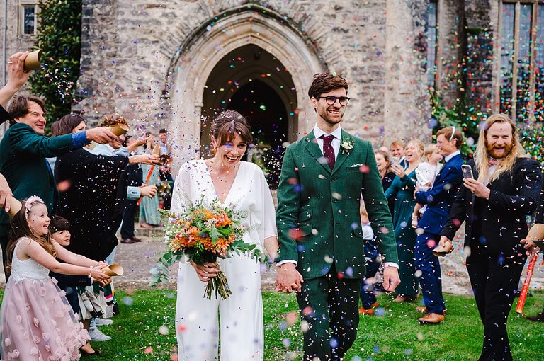 Bride and Groom walk through confetti at Dartington Hall - Blog Post - Average Wedding Photographer Cost