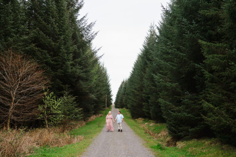 Standing tall but looking like ants surrounded by the very impressive pine tress at Bellever Forest by Cornwall Engagement Photographer, Jake Timms Photography
