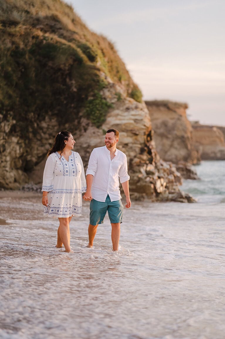 Wallking through shallow waters as the waves crash against the couples legs by Cornwall engagement photographer, Jake Timms Photography