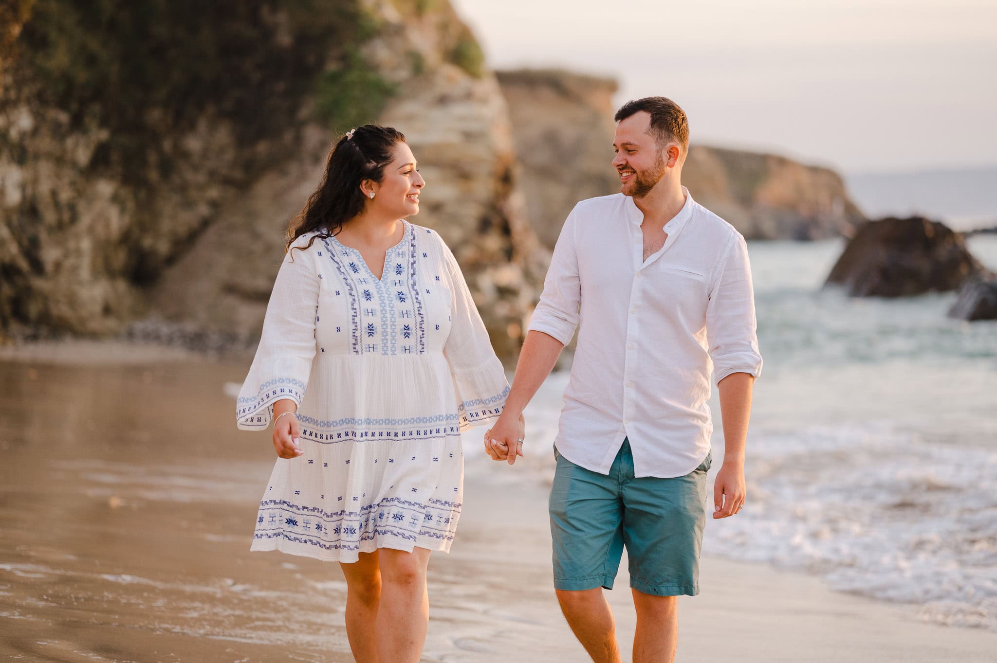 Looking into each other's eyes as the happy couple hold hands and walk along the beach