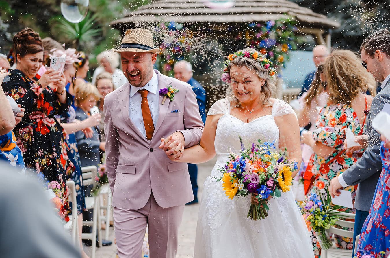 Newlyweds walk back down the wedding aisle being covered in colourful confetti at Tunnels by Devon Wedding Photographer, Jake Timms Photography