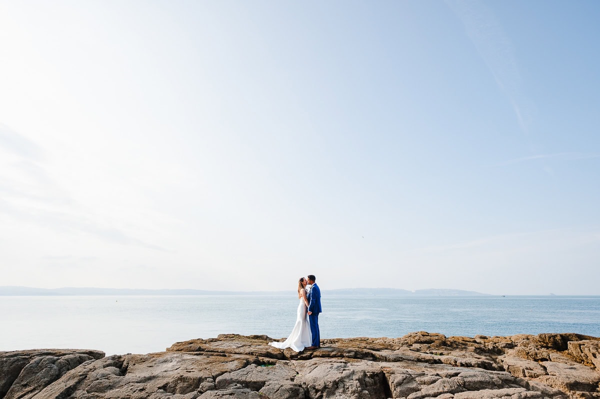 Standing on the rocky Devon coastline for the most breathtaking couple photos - Wedding Portfolio